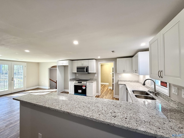 kitchen featuring appliances with stainless steel finishes, arched walkways, a sink, and light stone countertops