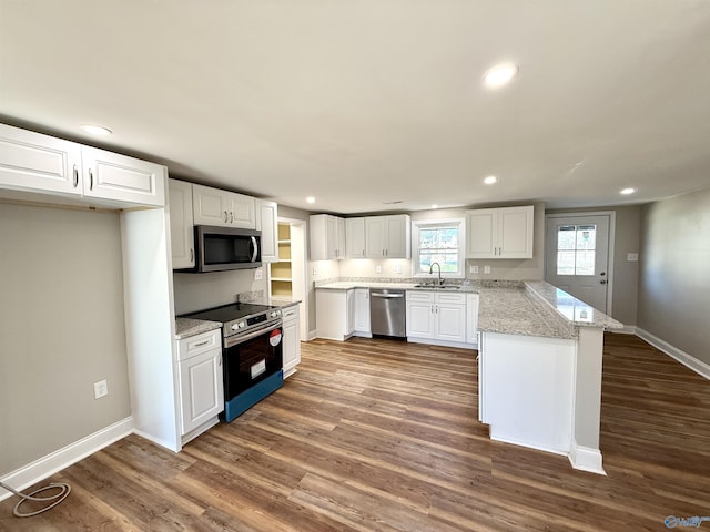 kitchen with a peninsula, appliances with stainless steel finishes, dark wood finished floors, and a sink