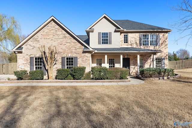 view of front facade with brick siding, roof with shingles, a front yard, and fence