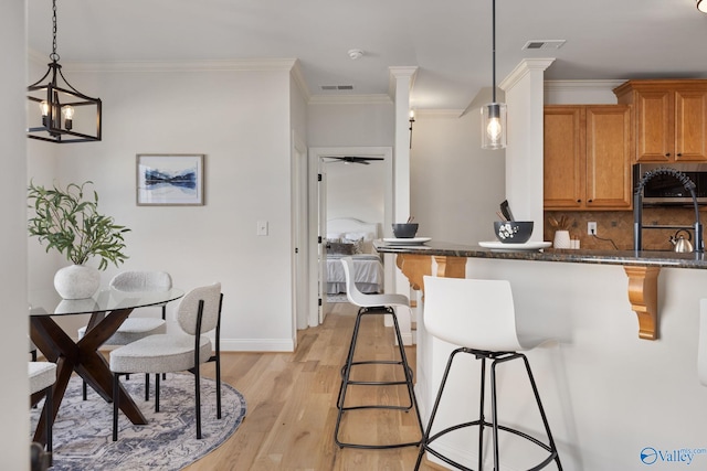 kitchen featuring tasteful backsplash, visible vents, stainless steel microwave, a breakfast bar area, and light wood-style floors