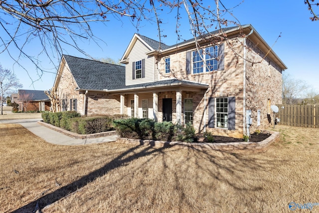 view of front of house featuring brick siding, covered porch, a front yard, and fence