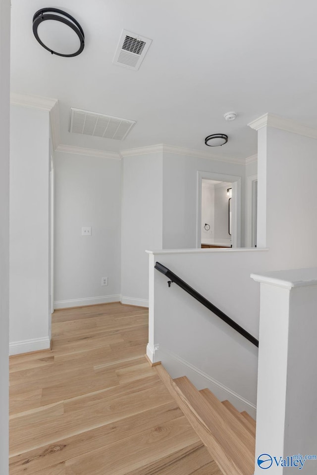 corridor with baseboards, visible vents, light wood finished floors, and ornamental molding