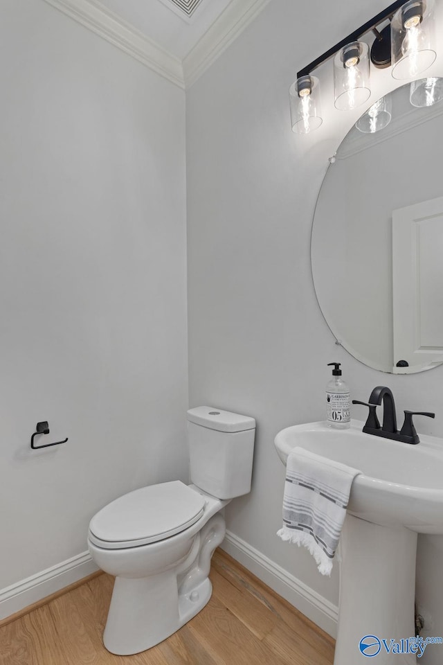 bathroom with toilet, wood finished floors, baseboards, and ornamental molding