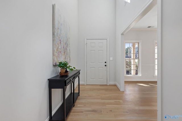 entryway with visible vents, a high ceiling, crown molding, light wood finished floors, and baseboards