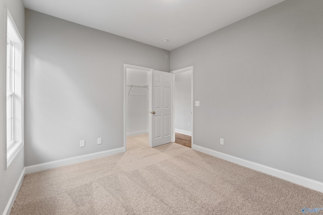 unfurnished bedroom with a walk in closet, light colored carpet, and a closet