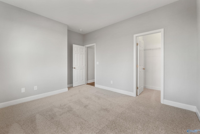 unfurnished bedroom featuring a walk in closet, light colored carpet, and a closet