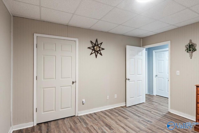 unfurnished bedroom with wood walls, a paneled ceiling, and hardwood / wood-style flooring