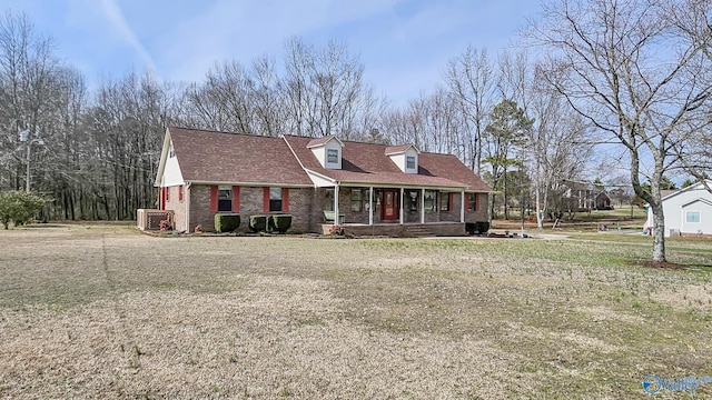 new england style home with covered porch, roof with shingles, a front lawn, and brick siding