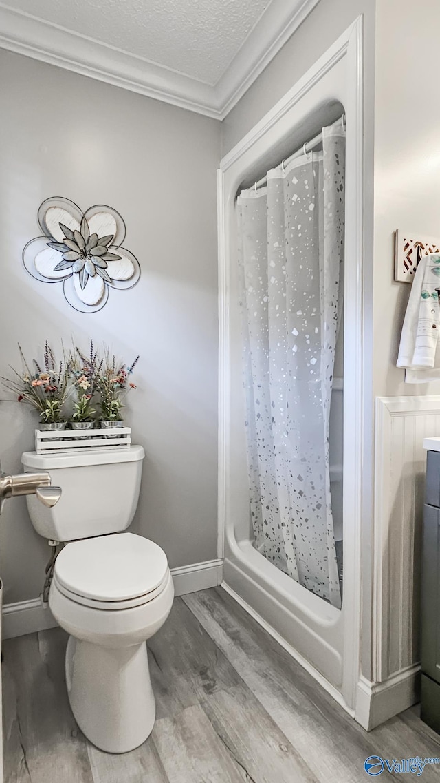 full bath featuring a textured ceiling, toilet, wood finished floors, ornamental molding, and a shower with curtain