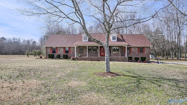 new england style home featuring a porch, brick siding, and a front lawn