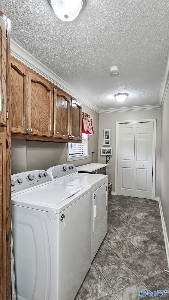 washroom with a textured ceiling, baseboards, ornamental molding, cabinet space, and washing machine and clothes dryer