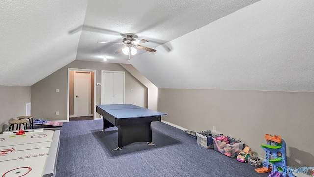 recreation room with lofted ceiling, dark carpet, ceiling fan, a textured ceiling, and baseboards