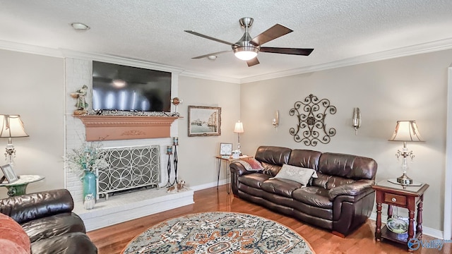 living area with ornamental molding, a fireplace, wood finished floors, and a ceiling fan