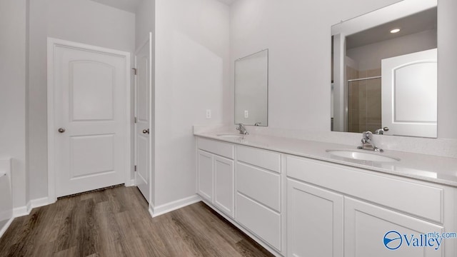 full bathroom with double vanity, a sink, a shower stall, and wood finished floors