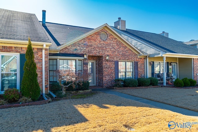 view of front facade with roof with shingles, a chimney, and brick siding