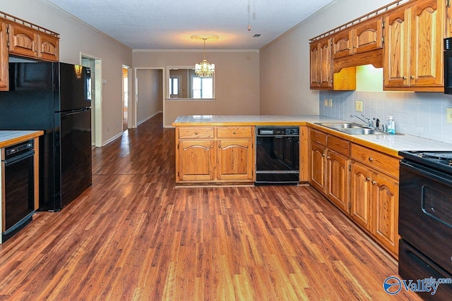 kitchen featuring crown molding, light countertops, a sink, a peninsula, and black appliances