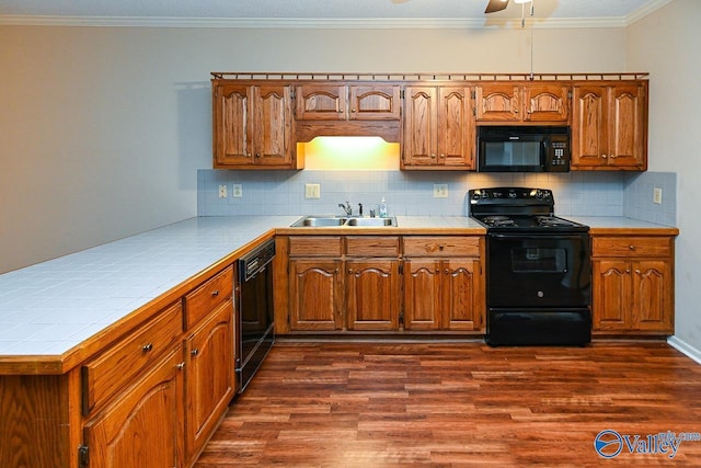 kitchen with dark wood-style floors, crown molding, tile counters, a sink, and black appliances