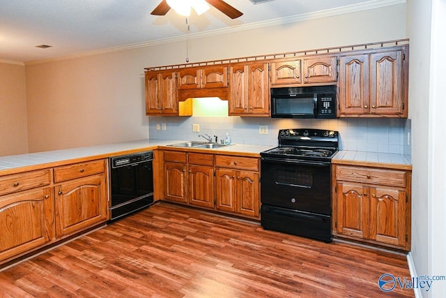 kitchen featuring tile counters, dark wood-style floors, ornamental molding, black appliances, and a sink