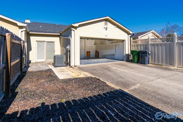 garage featuring driveway, central AC unit, and fence