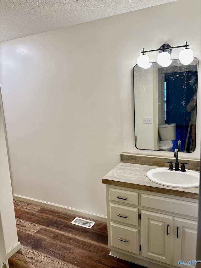 bathroom featuring vanity, toilet, wood-type flooring, and a textured ceiling