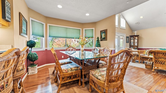 dining room featuring light wood-type flooring, lofted ceiling, and a textured ceiling