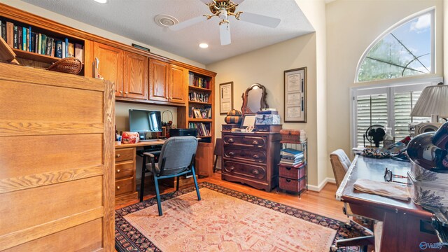 office space featuring built in desk, ceiling fan, light hardwood / wood-style floors, and a textured ceiling