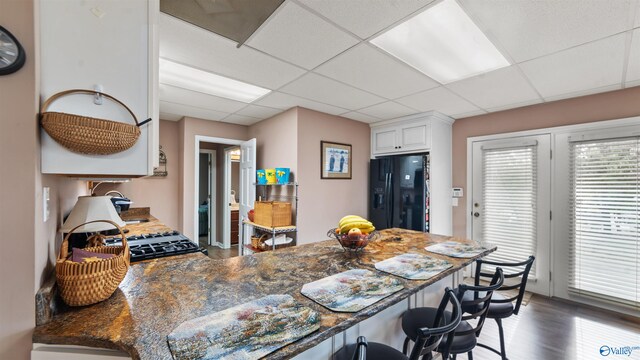 kitchen featuring dark hardwood / wood-style flooring, black refrigerator with ice dispenser, white cabinets, dark stone counters, and a drop ceiling