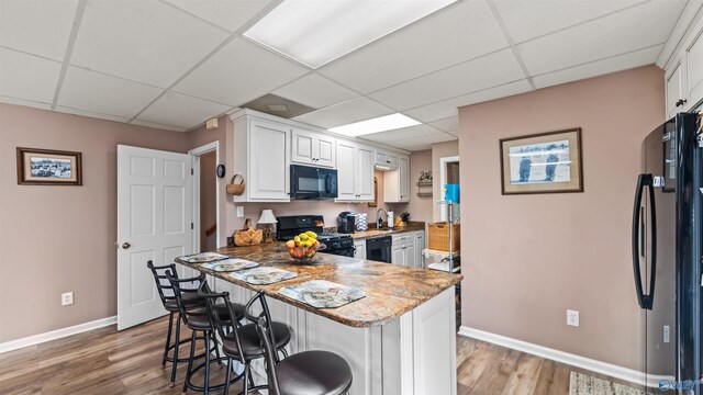 kitchen featuring black appliances, hardwood / wood-style floors, white cabinets, and a drop ceiling