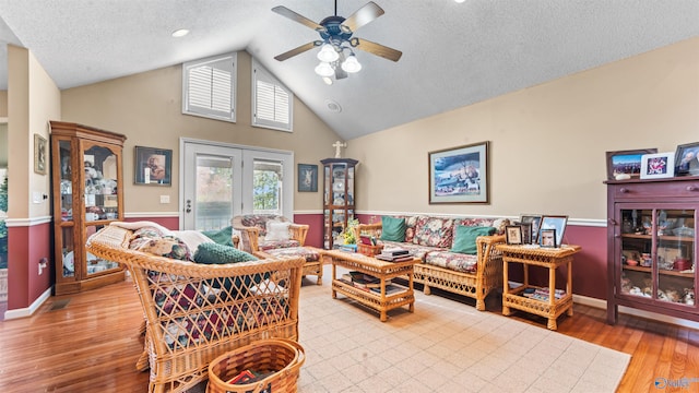 living room with light wood-type flooring, ceiling fan, a textured ceiling, and vaulted ceiling