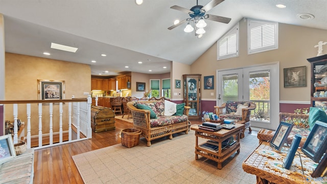 living room with high vaulted ceiling, light hardwood / wood-style flooring, a skylight, and ceiling fan