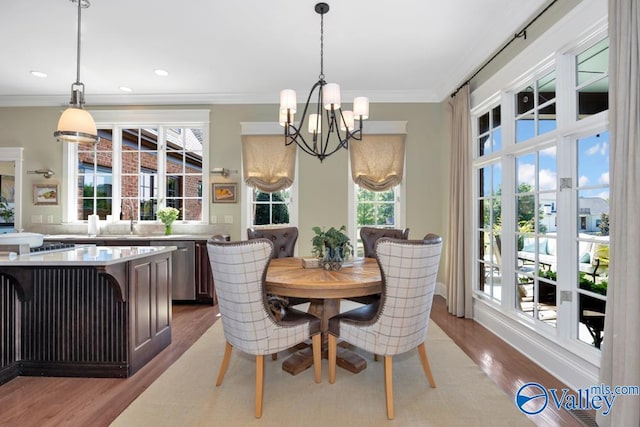 dining area with light hardwood / wood-style flooring, ornamental molding, sink, and an inviting chandelier