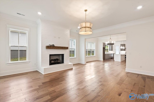 unfurnished living room featuring a brick fireplace, wood-type flooring, and ornamental molding