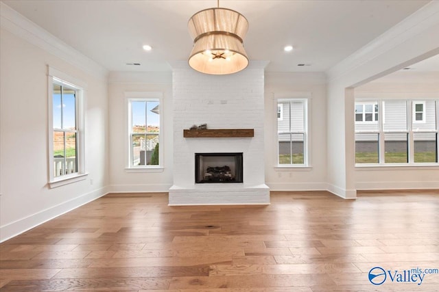 unfurnished living room featuring hardwood / wood-style flooring, ornamental molding, and a brick fireplace