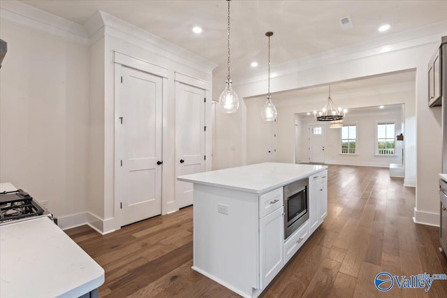 kitchen featuring hanging light fixtures, dark hardwood / wood-style floors, stainless steel microwave, white cabinets, and a kitchen island