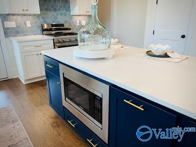 kitchen with blue cabinetry, white cabinets, stainless steel appliances, hardwood / wood-style floors, and backsplash