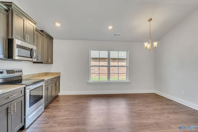 kitchen with light stone countertops, appliances with stainless steel finishes, dark wood-type flooring, an inviting chandelier, and hanging light fixtures