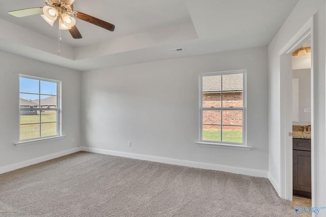 carpeted spare room with a raised ceiling, ceiling fan, and a healthy amount of sunlight