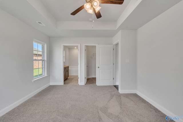 unfurnished bedroom featuring ceiling fan, a raised ceiling, light carpet, and ensuite bath