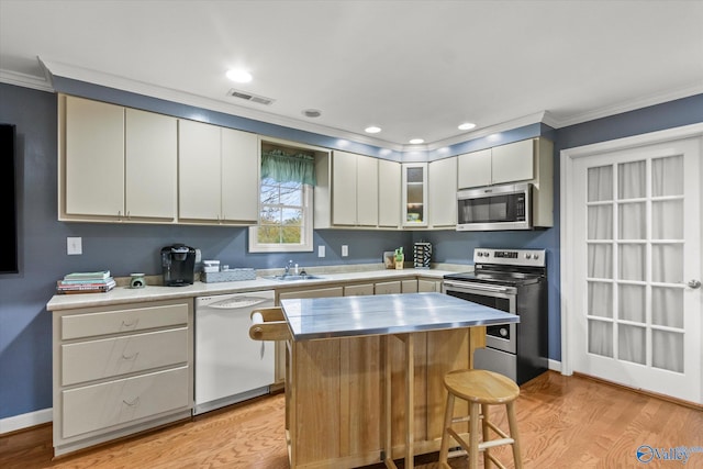 kitchen with a kitchen breakfast bar, crown molding, light wood-type flooring, appliances with stainless steel finishes, and a kitchen island