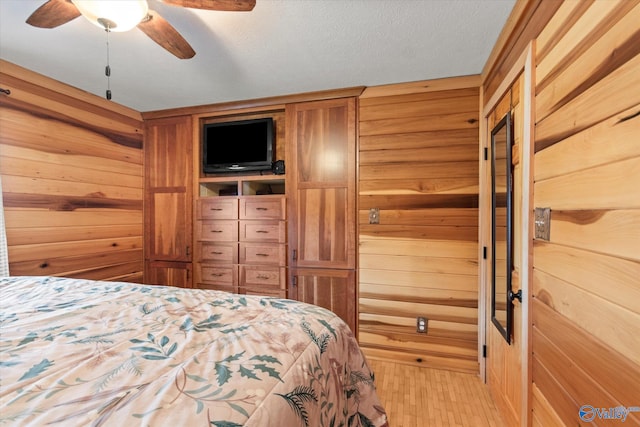 bedroom featuring a textured ceiling, light hardwood / wood-style flooring, ceiling fan, and wood walls