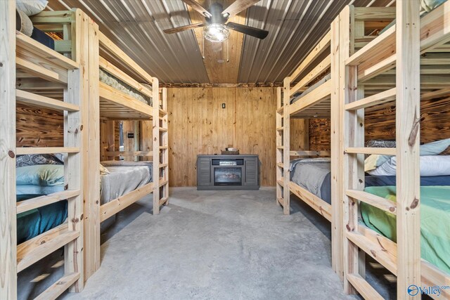 bedroom featuring ceiling fan, wooden walls, and concrete floors