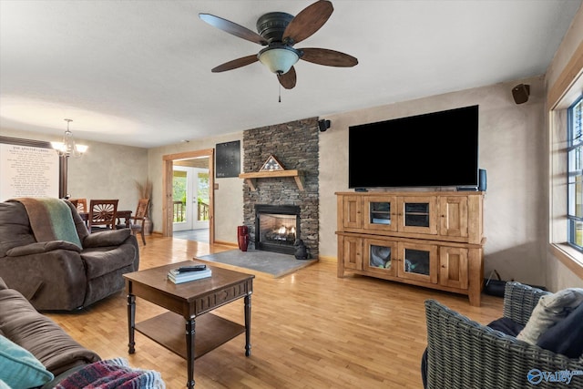 living room with ceiling fan with notable chandelier, a fireplace, and light hardwood / wood-style flooring