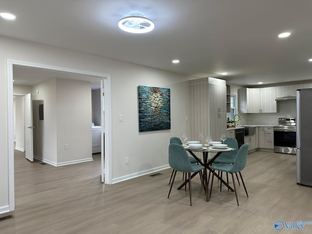 dining area featuring washer / dryer, sink, and light hardwood / wood-style flooring