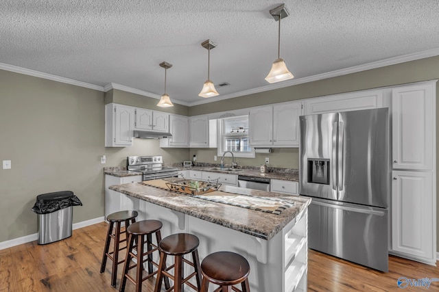 kitchen with appliances with stainless steel finishes, ornamental molding, pendant lighting, white cabinets, and a kitchen island