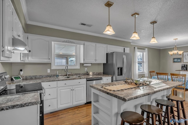 kitchen featuring appliances with stainless steel finishes, ornamental molding, a textured ceiling, white cabinets, and a center island