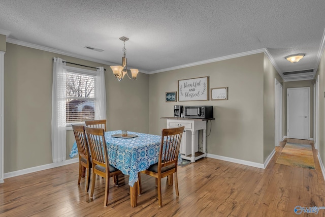 dining space with a textured ceiling, light wood-type flooring, crown molding, and an inviting chandelier