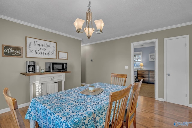 dining room featuring a chandelier, light wood-type flooring, a textured ceiling, and crown molding