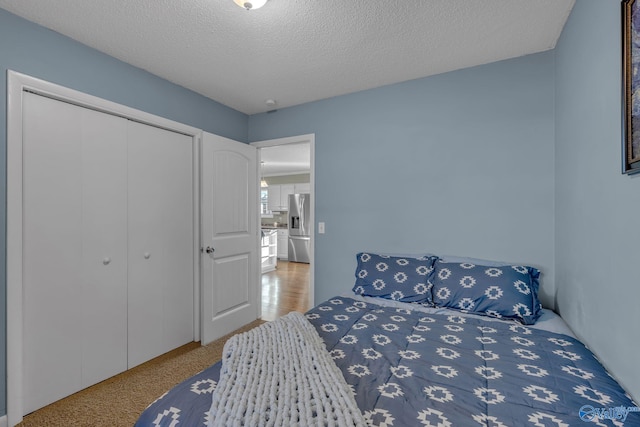 bedroom with a textured ceiling, a closet, and stainless steel refrigerator with ice dispenser