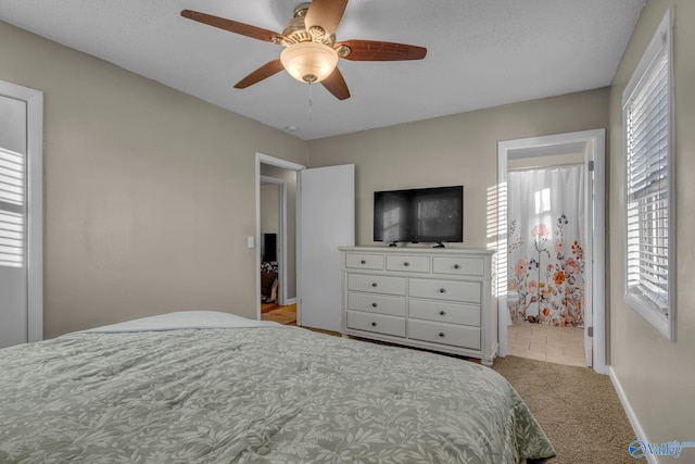 bedroom with ceiling fan, light colored carpet, a textured ceiling, and connected bathroom