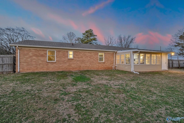 back house at dusk with a sunroom and a yard